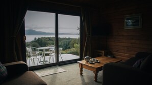 Een gezellige kamer met een grote schuifglazen deur die uitkomt op een balkon. Binnen staat een houten tafel met een theepot en kopjes, een bank en een stoel.