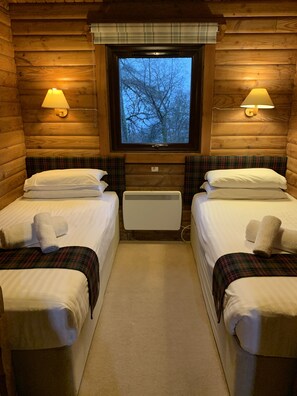 A cabin-style room with two single beds, plaid bedding, a window with a view of trees, and wall-mounted lamps. - Armadale Castle Cabins (Sleat)