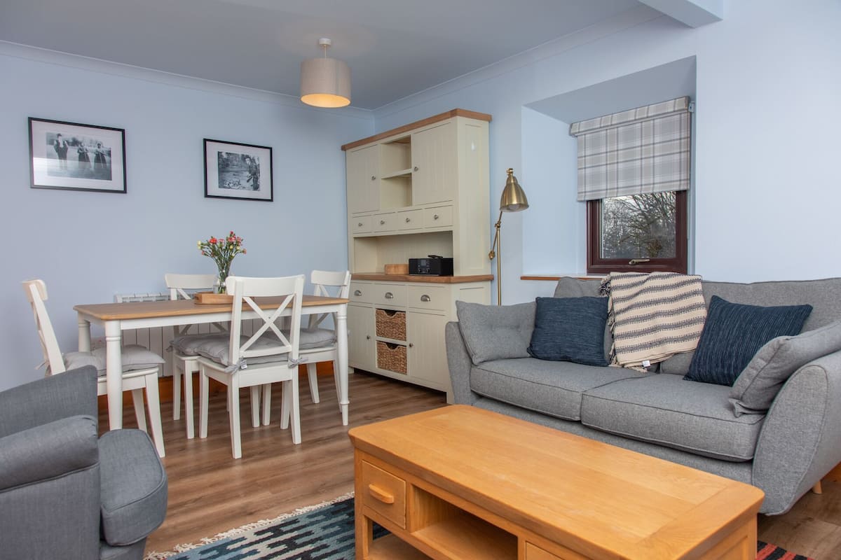 A cozy living room with a grey sofa, a wooden coffee table, and a dining area with a white table and chairs.