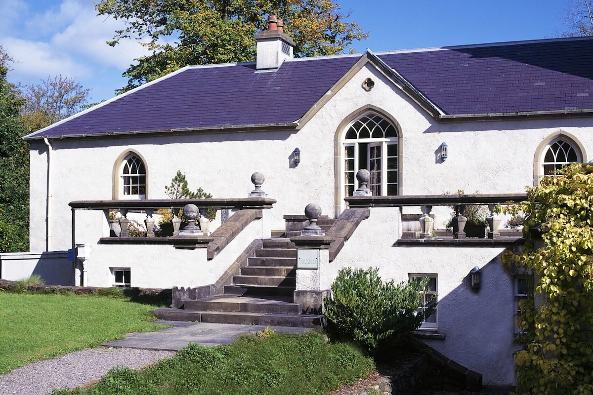 A white building with a dark roof, a stone staircase, and a small garden area.
