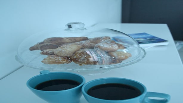 A clear glass bowl with pastries on a white table, accompanied by two blue cups of coffee. - Mayfair Holiday Apartment (London)