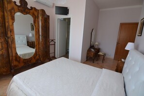 Un dormitorio con una cama grande, un armario de madera con espejo, un televisor y una puerta que da a otra habitación.