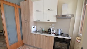 A compact kitchen with a gas stove, oven, and a small sink. There are cabinets above the countertop and a microwave to the right. - B&B Domus Lupiae (Lecce)
