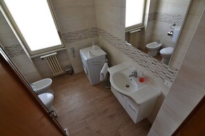 Un baño con inodoro, bidé y lavamanos, paredes con azulejos y una ventana.