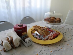 A table with a yellow plate of pastries, a glass container of cookies, and a glass dome of muffins. - B&B Domus Lupiae (Lecce)