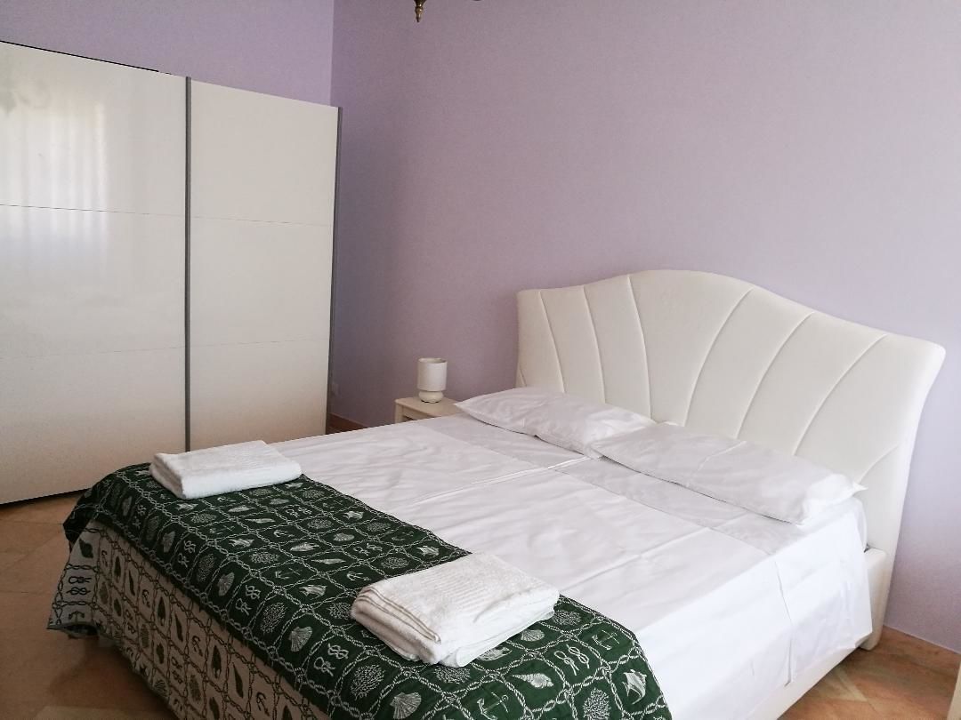 A neatly made bed with white linens, a green patterned bedspread, and a white headboard.