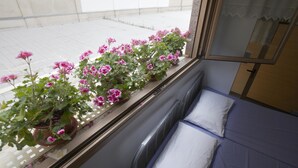 A room with a window sill lined with potted pink flowers, a bed with white pillows, and a view of a tiled outdoor area. - Albergue Albas - Hostel (Logroño)