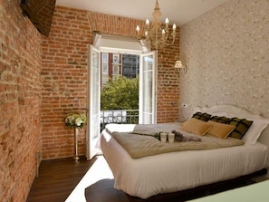 Un dormitorio con pared de ladrillo, una cama grande, una araña y vistas al exterior.