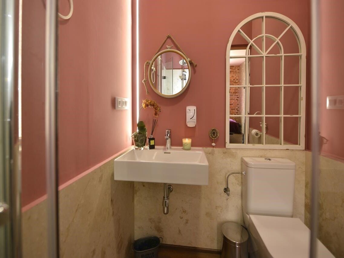 Un baño con un lavabo blanco, un espejo redondo, una ventana con marco blanco y un inodoro.