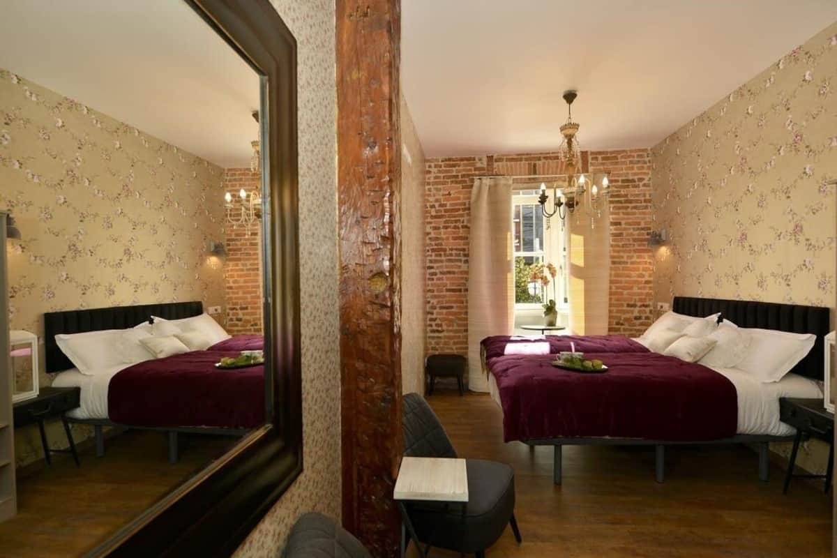 A room with two beds, a mirror, a chandelier, and a window with curtains.