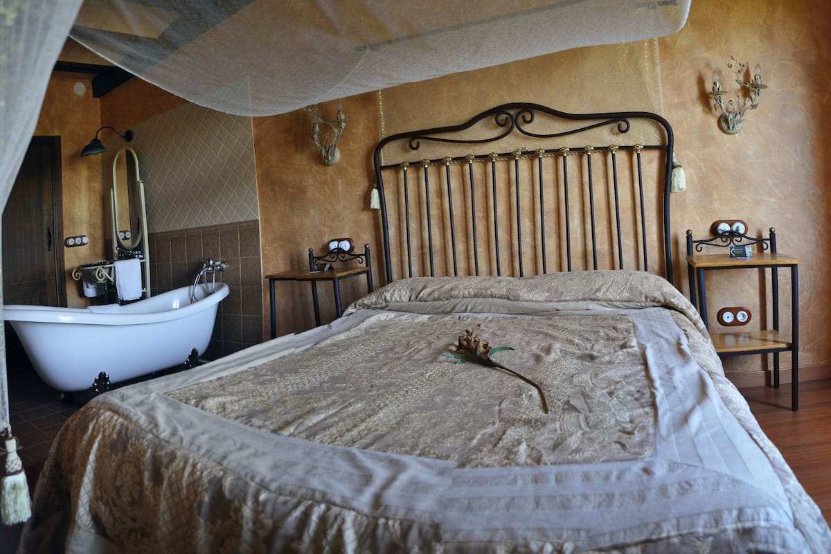Une chambre à coucher avec un grand lit, une tête de lit en bois, une table de chevet, une horloge murale et une baignoire.