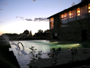 A swimming pool with a water feature, a stone building with large windows, and a view of the sky. - Hotel con encanto - SPA Kinédomus Bienestar (Fresnillo de las Dueñas)