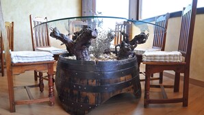 A rustic wooden table with a glass top, surrounded by chairs with white cushions. - Hotel con encanto - SPA Kinédomus Bienestar (Fresnillo de las Dueñas)