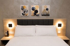 A hotel room with a bed, two bedside tables, and three wall-mounted artworks.