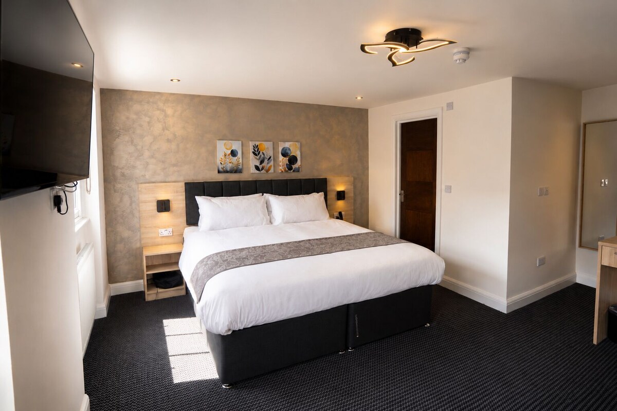 A hotel room with a large bed, bedside tables, a flat-screen TV, and artwork on the wall.