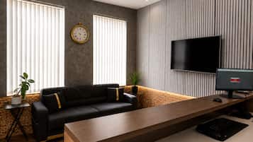 Uma sala de estar moderna com sofá, mesa de centro de madeira, televisão e relógio fixado na parede.