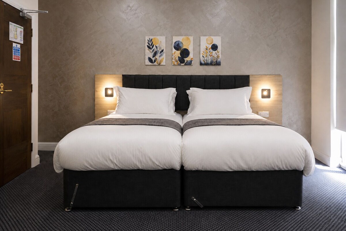 A double bed with a dark headboard and two bedside tables, each with a wall-mounted lamp.