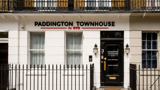 Un bâtiment blanc avec une porte d’entrée noire portant l’inscription « PADDINGTON TOWNHOUSE by OYO ».