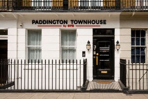Ein weißes Gebäude mit einer schwarzen Eingangstür, auf der 'PADDINGTON TOWNHOUSE by OYO' steht.