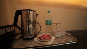 Una bandeja con una tetera de acero inoxidable, una botella de agua, dos tazas blancas y un plato con porciones de aperitivos.