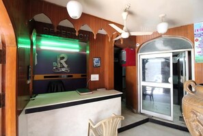 Zona de recepción con escritorio, sillas, ventilador de techo y puerta de vidrio que da al exterior.