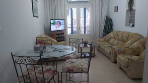A living room with a round glass table, two chairs, a sofa, and a television. - El Goulli Appartement (Hergla)