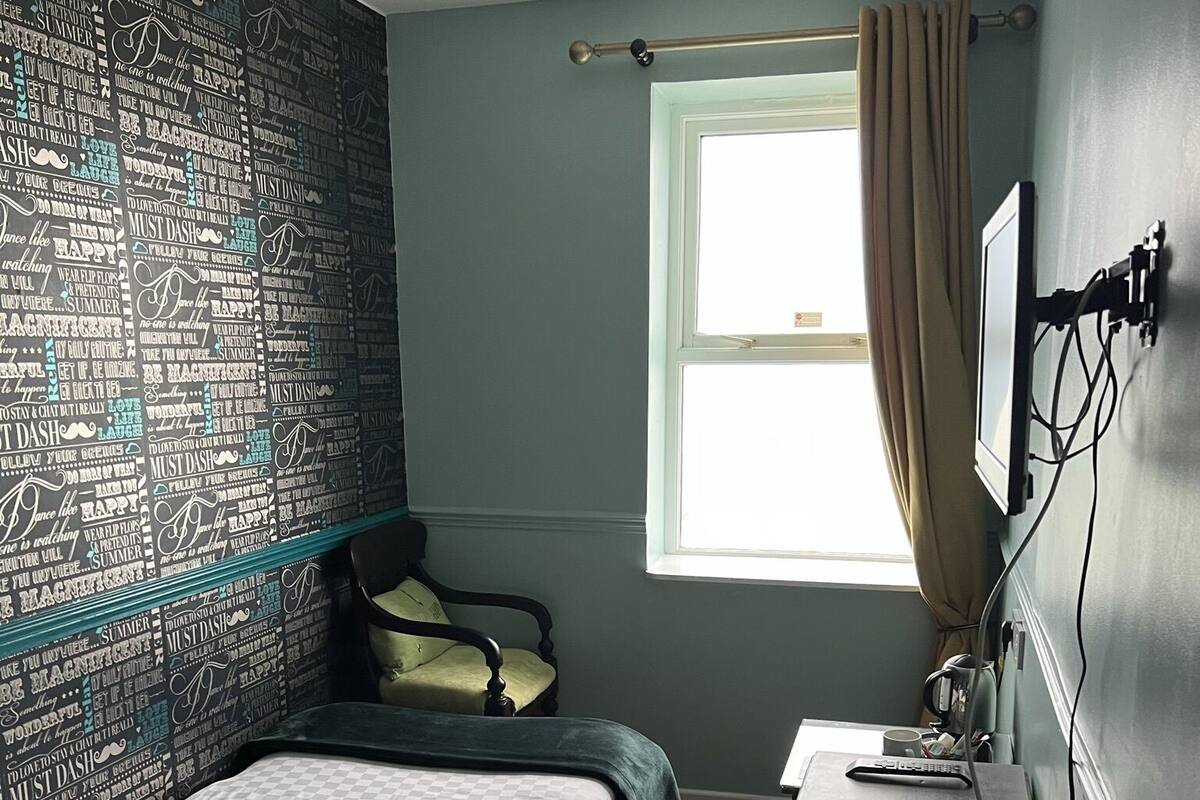 A bedroom with a bed, a desk, a radiator, and a window with curtains.
