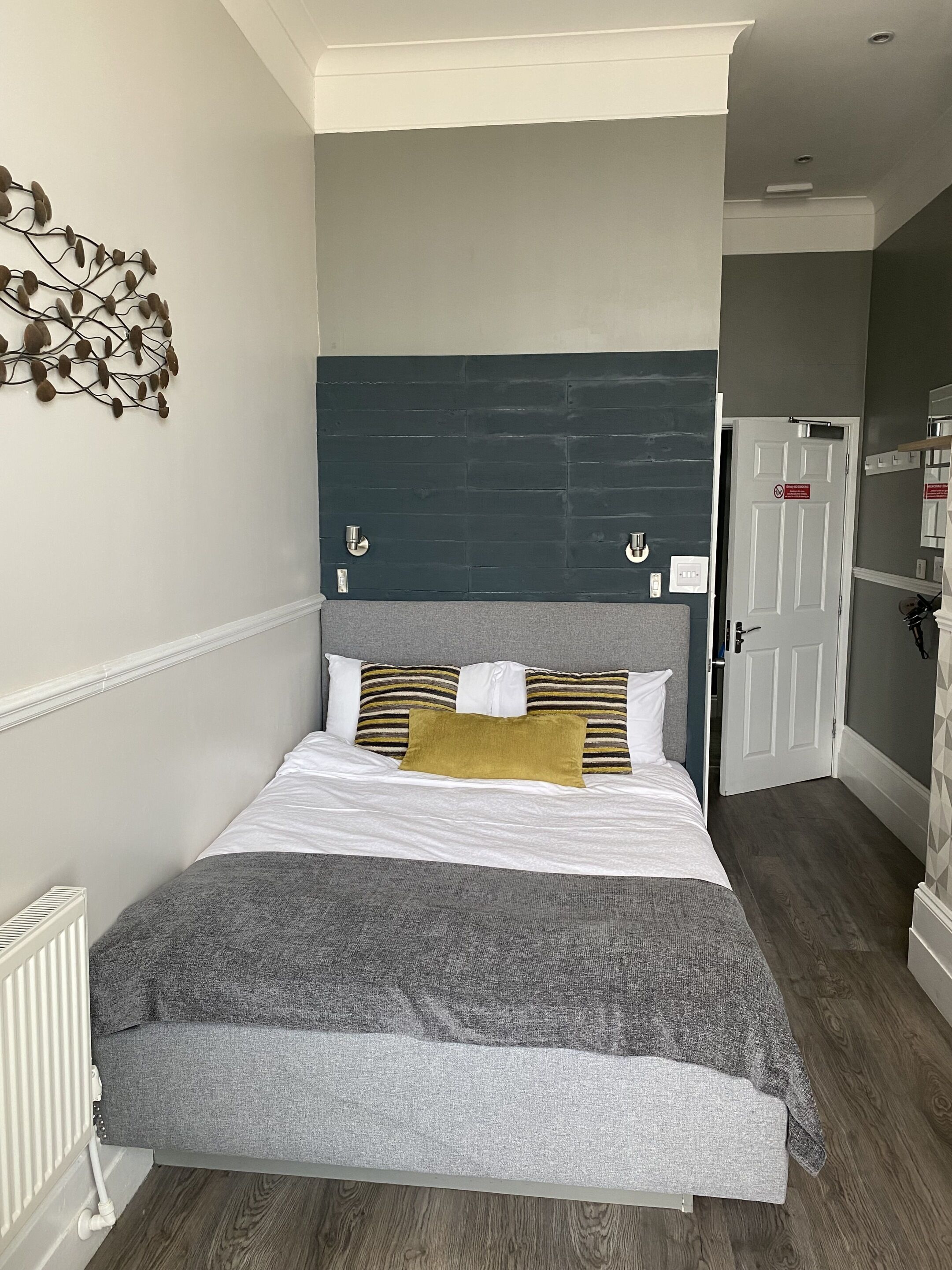 A neatly made bed with a grey and white duvet, a mustard-colored pillow, and striped pillows.