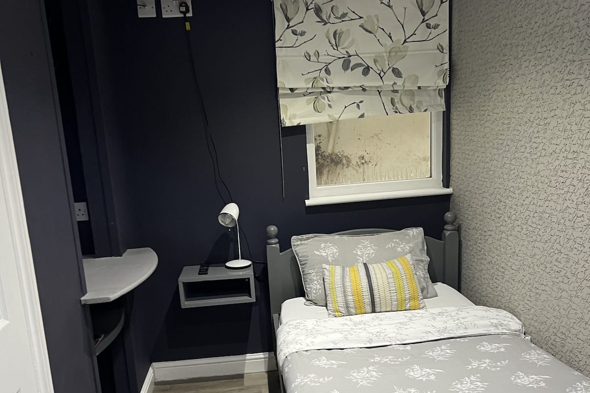 A bedroom with a bed, bedside table, and a window with a curtain.