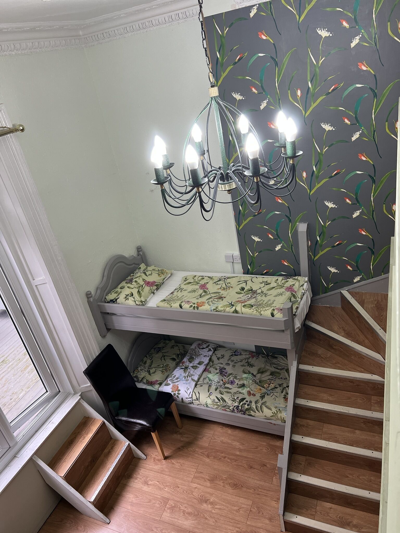 A bunk bed with floral bedding, a chandelier, and a staircase.