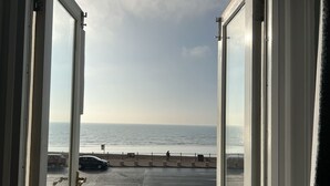 A view from a window overlooking a beach with a road and a pedestrian path. - Astral Lodge (Hastings)