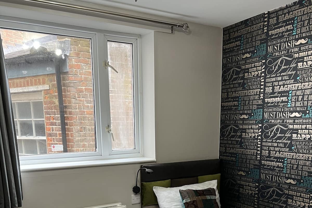 A bedroom with a bed, a window, a radiator, and a wall with motivational quotes.