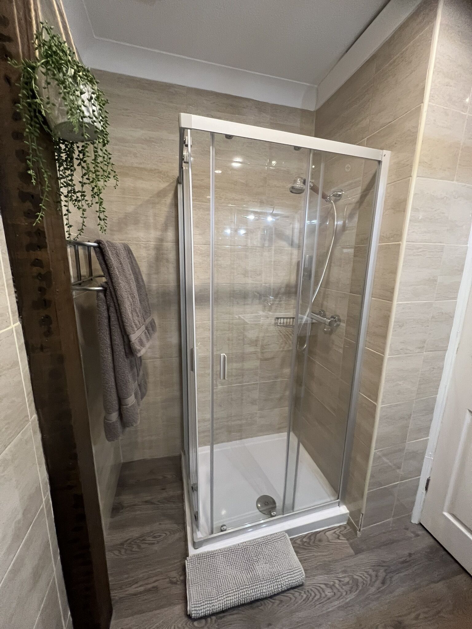 A glass-enclosed shower with a tiled floor and a towel rack with towels.