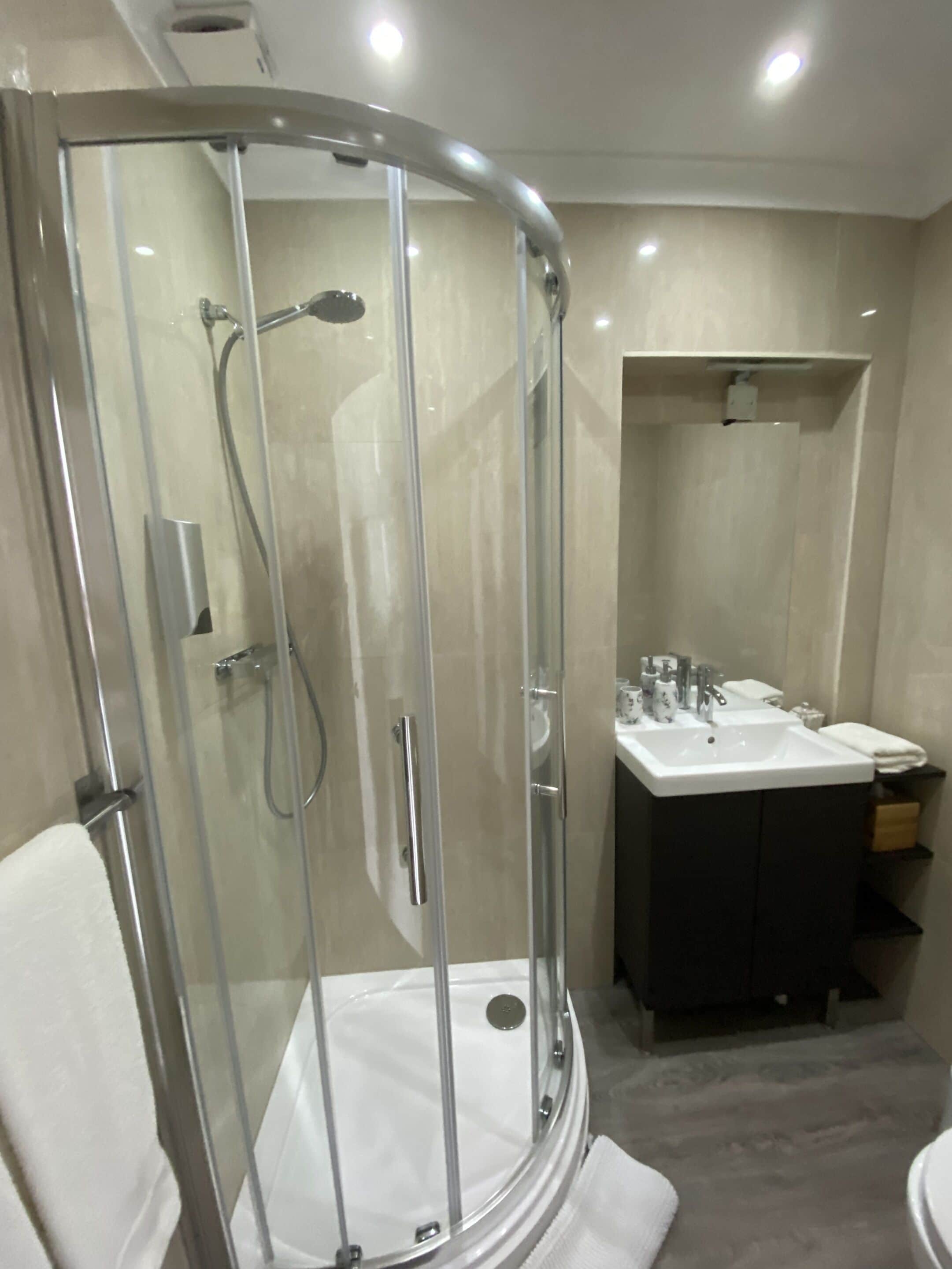A modern bathroom with a glass-enclosed shower, a white sink, and a dark vanity.