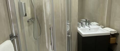A modern bathroom with a glass-enclosed shower, a white sink, and a dark vanity.