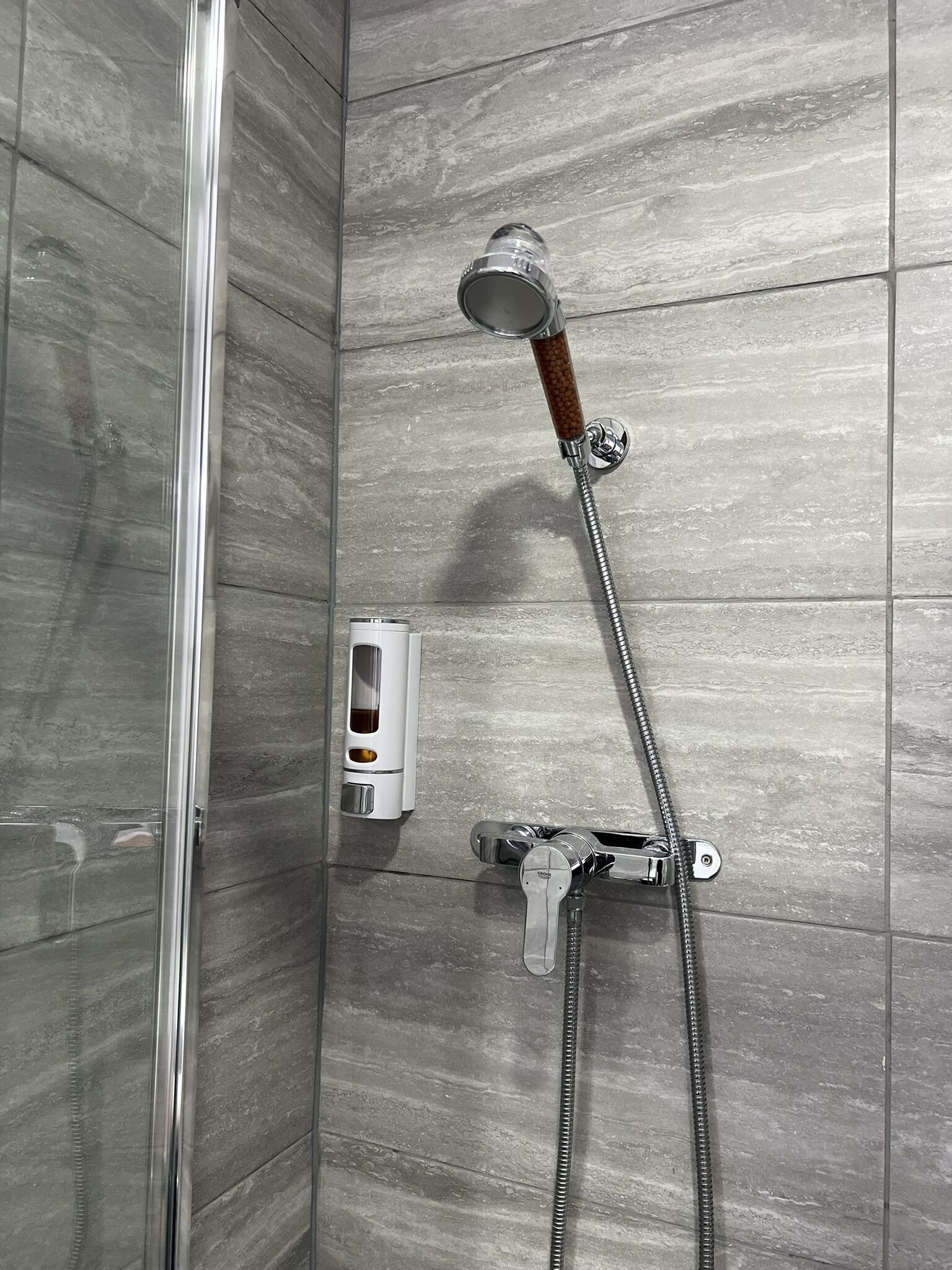 A shower with a wooden handle, a soap dispenser, and a chrome faucet.