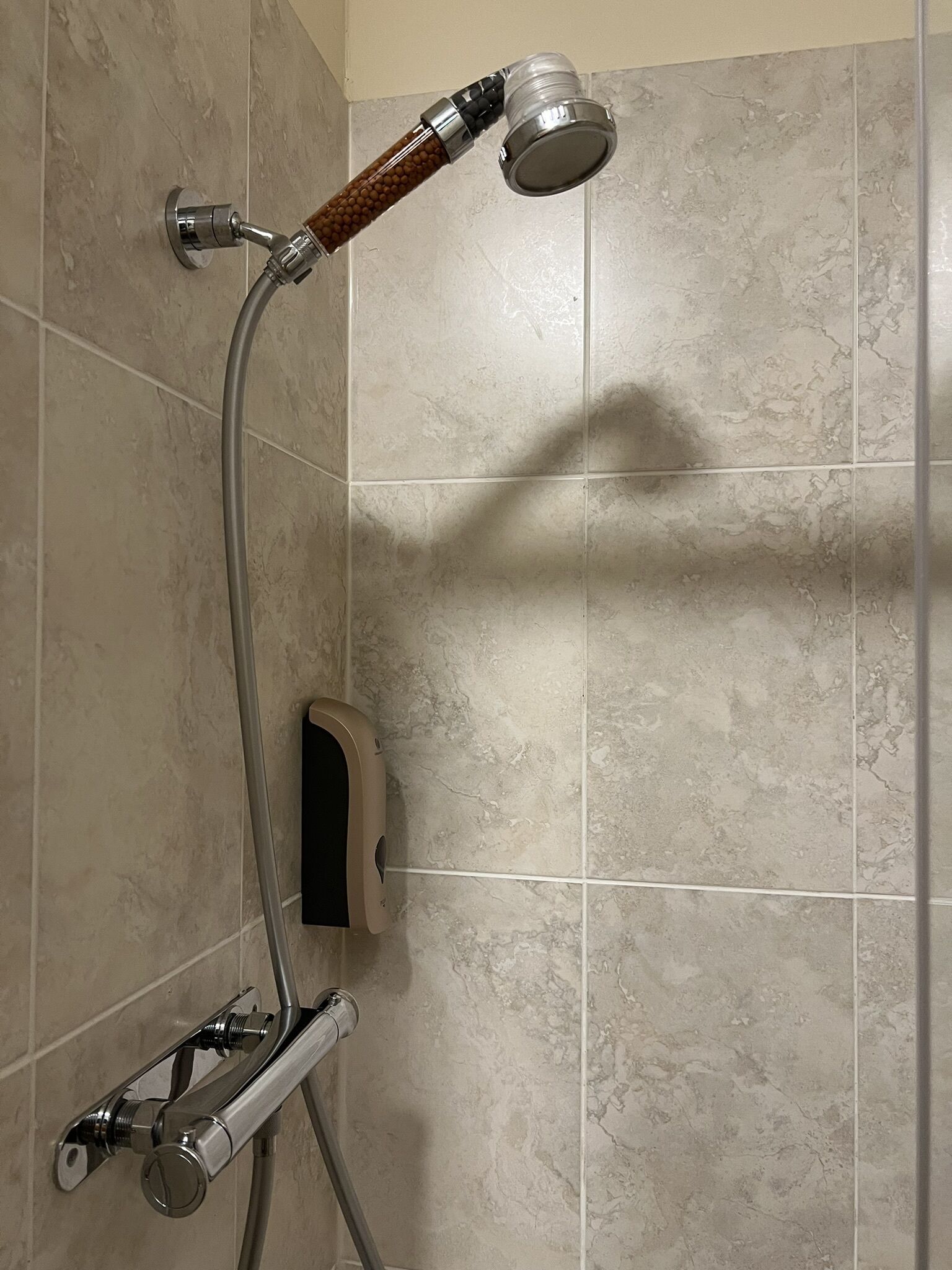 A shower with a handheld showerhead, a handheld shower attachment, and a wall-mounted faucet.