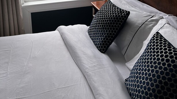 A hotel room with a bed, a nightstand, a lamp, and a view of the sea through a large window. - Astral Lodge (Hastings)