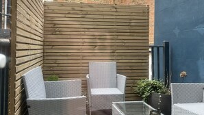 A patio area with wicker furniture and a glass table, surrounded by a wooden fence and a brick wall. - Astral Lodge (Hastings)