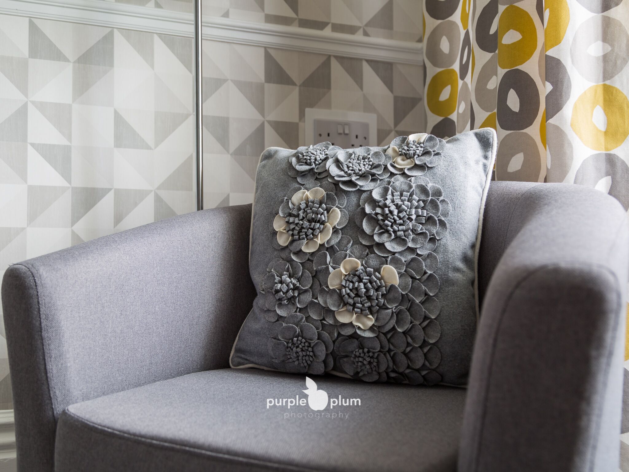 A grey armchair with a decorative pillow featuring a floral pattern.