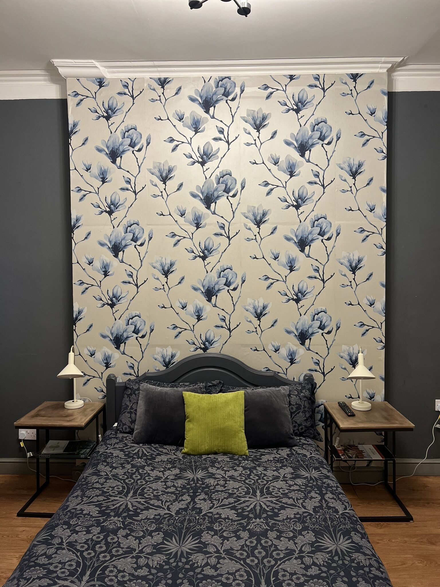 A bedroom with a floral wallpaper, a dark patterned bedspread, and two bedside tables with lamps.