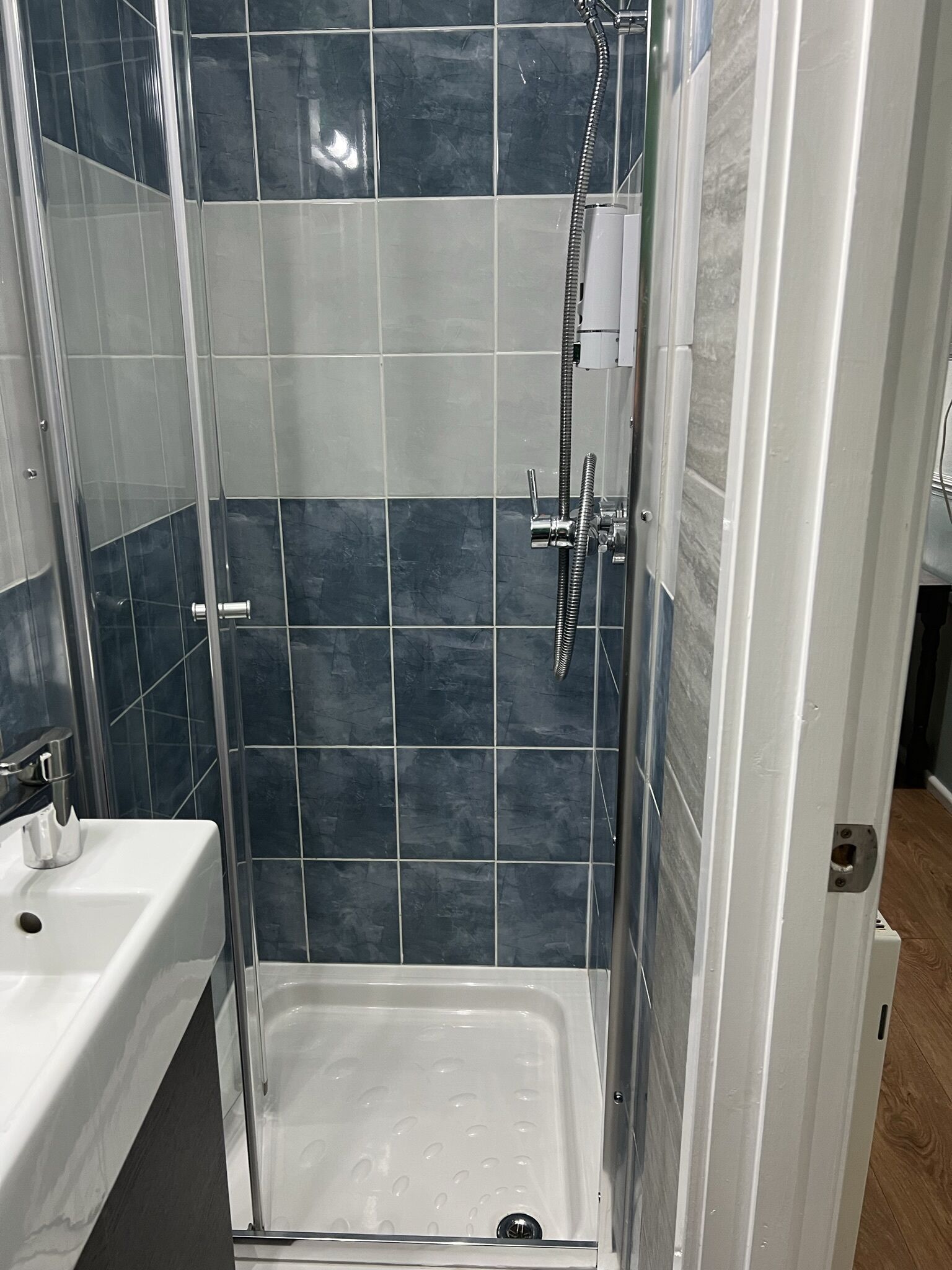 Une cabine de douche dotée d’une porte en verre, d’un lavabo blanc et d’un mur carrelé orné d’un motif bleu foncé.