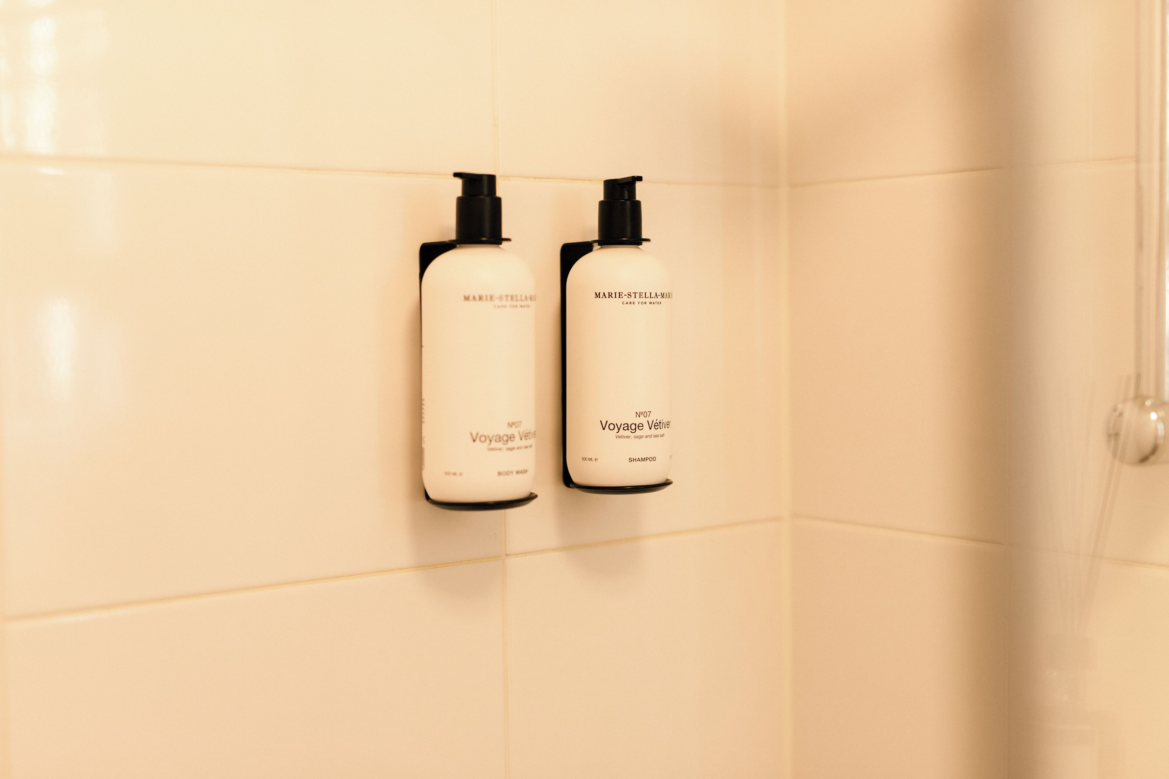 Two Marie-Stella Voyage Vatti shampoo bottles mounted on a tiled wall.