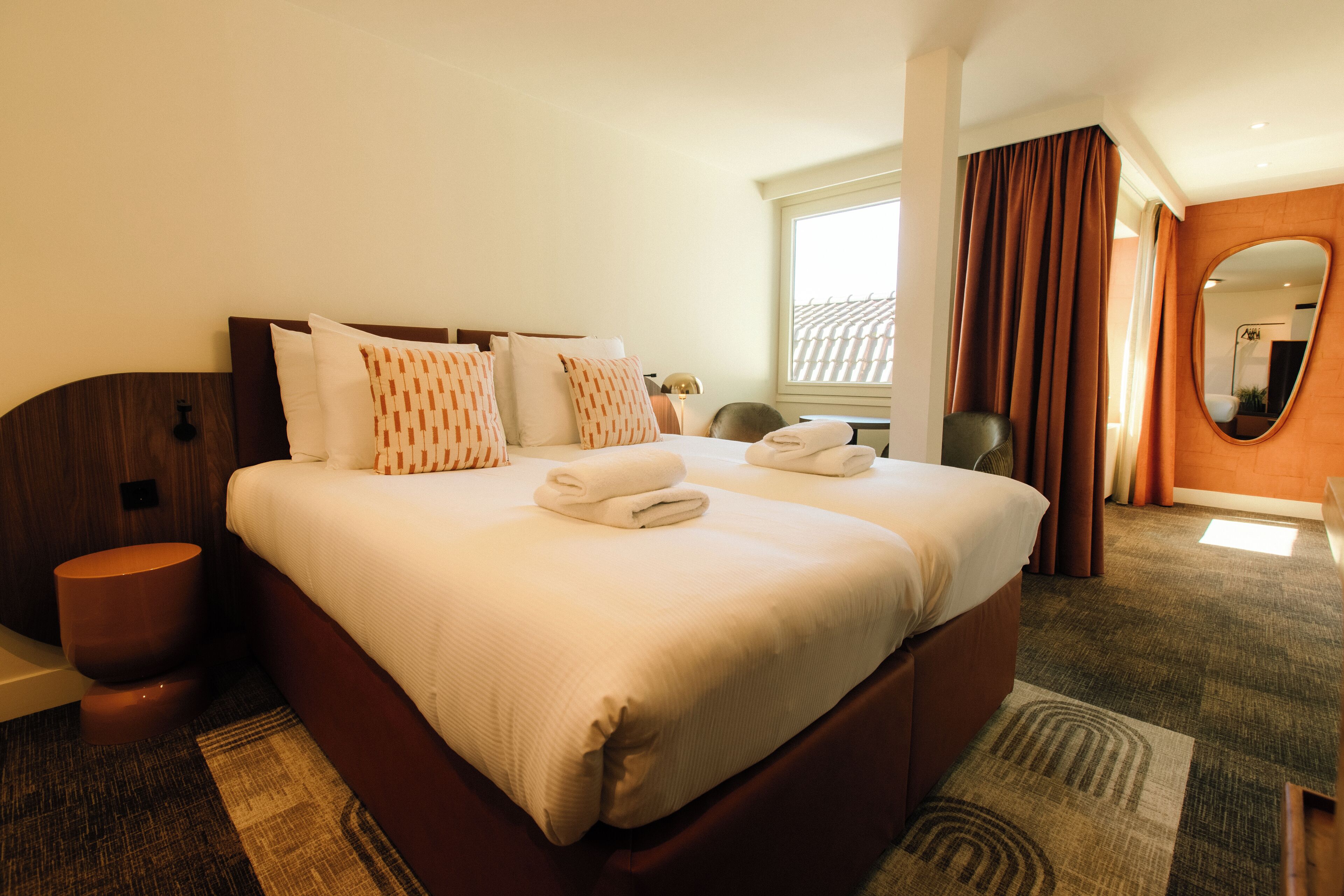 Ein Hotelzimmer mit einem großen Bett, einem Nachttisch, einem Spiegel und einem Vorhangfenster.