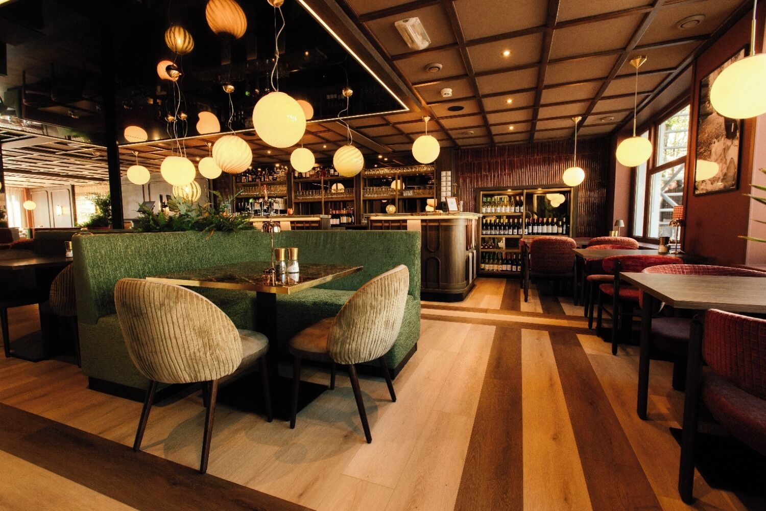 Zona de bar con una banca verde, mesas de madera y luces esféricas colgantes.