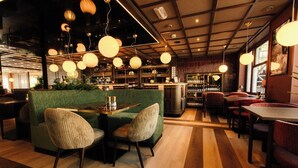 Un espace bar avec un coin salon vert, des tables en bois et des lampes sphériques suspendues.