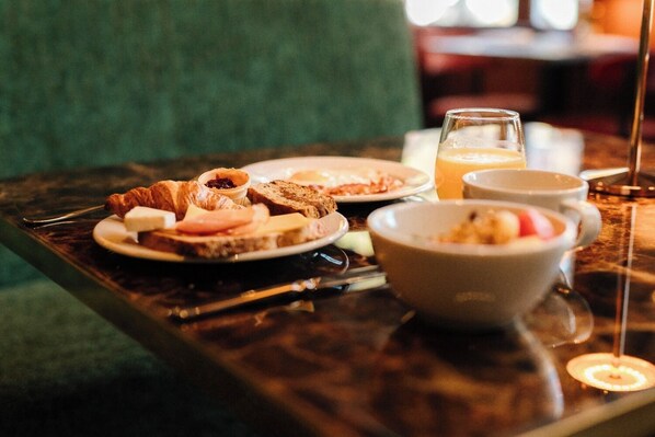 A breakfast table with plates of food, a bowl, and a glass of juice.