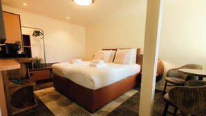 Une chambre d’hôtel comprenant un lit, un bureau avec une machine à café, une chaise et une petite table.