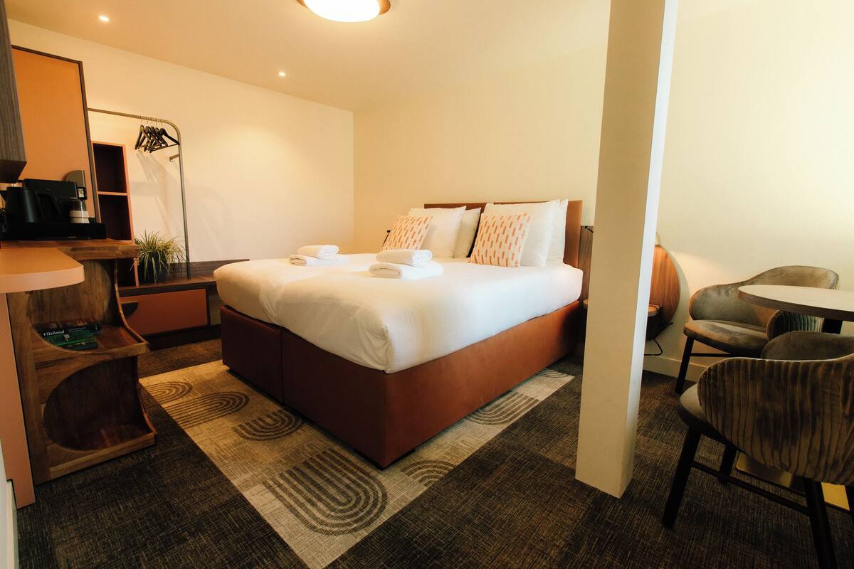 Une chambre d’hôtel comprenant un lit, un bureau avec une machine à café, une chaise et une petite table.