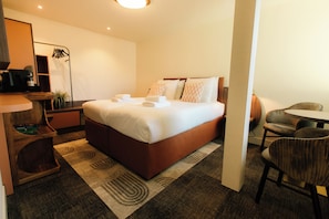 Une chambre d’hôtel comprenant un lit, un bureau avec une machine à café, une chaise et une petite table.